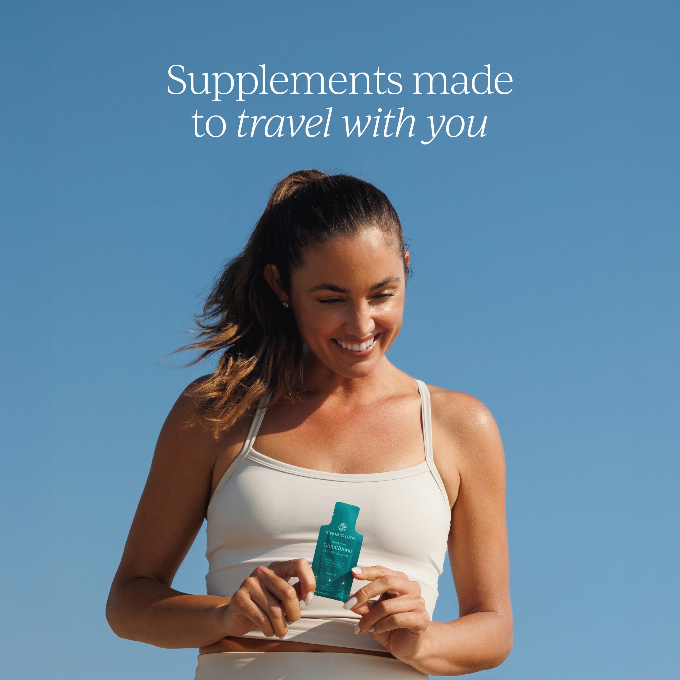 Woman outdoors holding a Cymbiotika Glutathione sachet — supplements made to travel with you